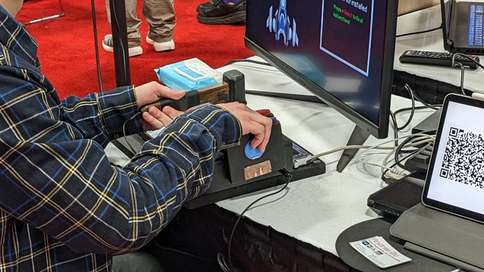 A player holds a hammer and two floppy discs on a custom controller board at GDC