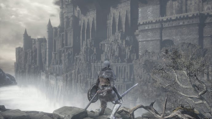 A character in Dark Souls in grey armour next to a grey tree looking towards a grey cliff with a grey castle on it